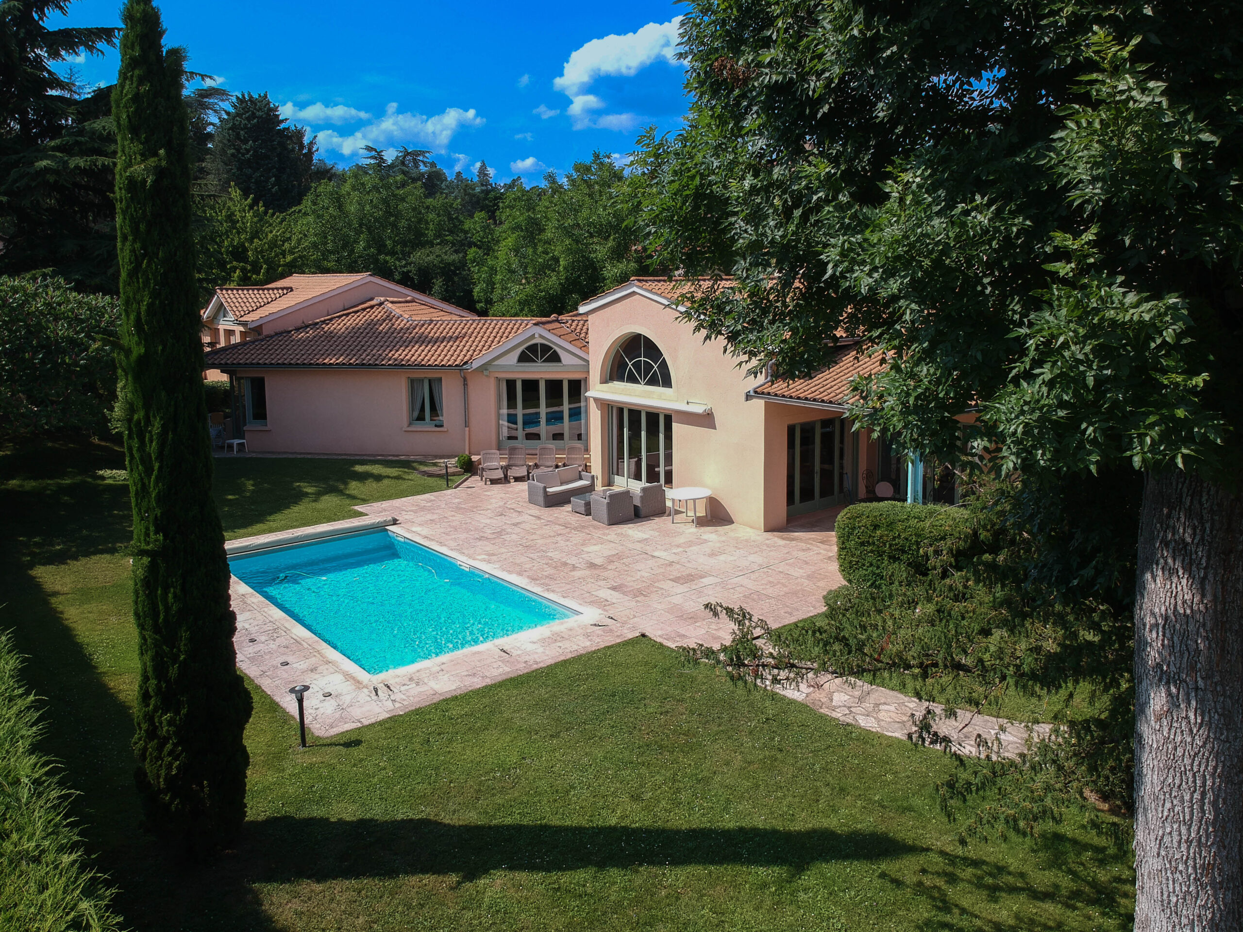 Vue de face d'une grande maison avec piscine entourée d'arbres, capturée par drone par l'agence de communication Glick, spécialisée en photographie immobilière Haut-Rhin